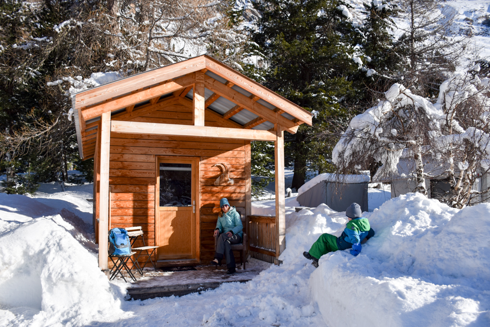 Winter Glamping Campingplatz Morteratsch Engadin Graubünden Schweiz Travel Sisi Esther Mattle mit Sohn vor dem Holzhaus